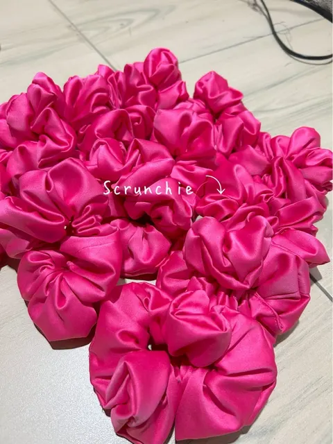 Tumpukan ikat rambut scrunchie satin merah muda terang di atas lantai keramik