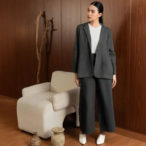Model memakai setelan blazer dan celana panjang abu tua bergaris dengan atasan putih, di ruang berpanel kayu