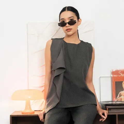 Model berkacamata hitam memakai atasan tanpa lengan abu tua bergaris dengan kain lipit di depan