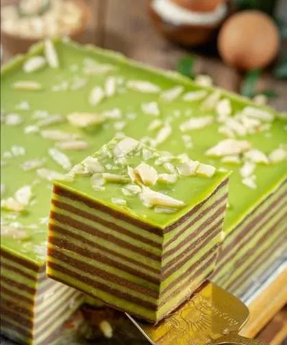 Potongan kue lapis berlapis hijau dan cokelat bertabur irisan almond di atas alas keemasan