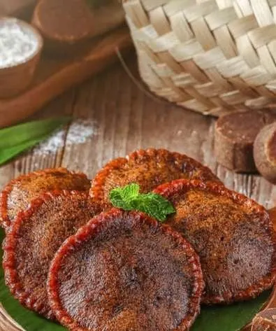 Beberapa kue cucur cokelat bulat bertumpuk di atas daun pisang dengan hiasan daun mint