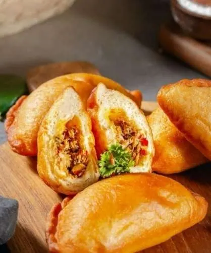 Panada goreng keemasan di atas papan kayu, satu dibelah dan menampilkan isian