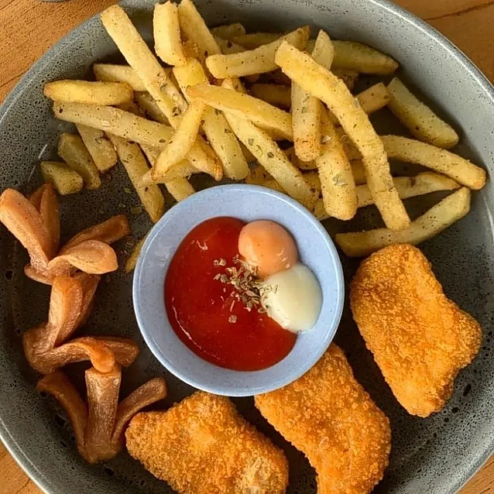 Piring abu-abu berisi kentang goreng, nugget, keripik dan mangkuk kecil saus merah dan mayones