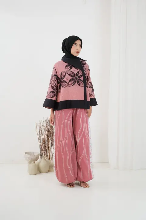 Model berhijab hitam memakai atasan batik merah muda bermotif hitam dan celana merah muda bermotif garis