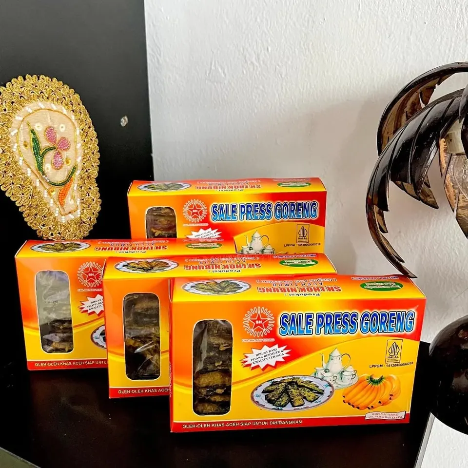 Empat kotak Sale Press Goreng berwarna kuning dan merah dengan jendela plastik, tersusun di atas meja hitam