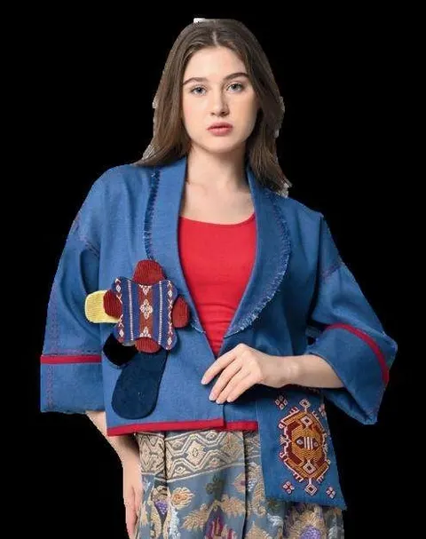 Model memakai jaket biru berlengan lebar dengan tempelan kain tenun merah dan biru di latar hitam