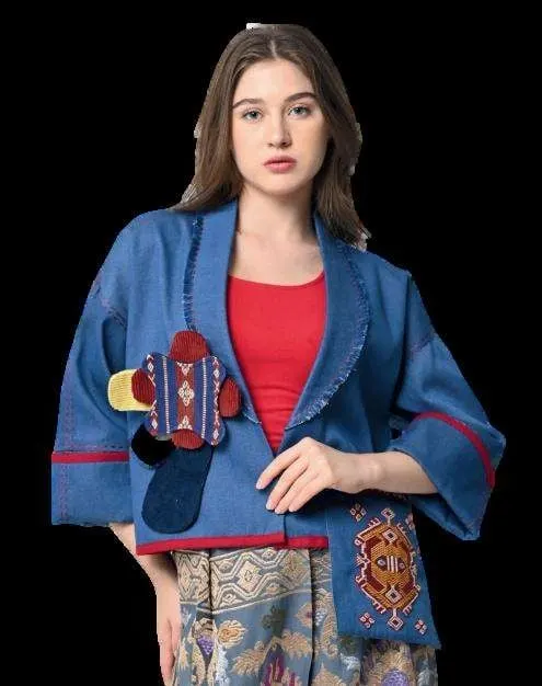 Model memakai jaket biru berlengan lebar dengan tempelan kain tenun merah dan biru di latar hitam