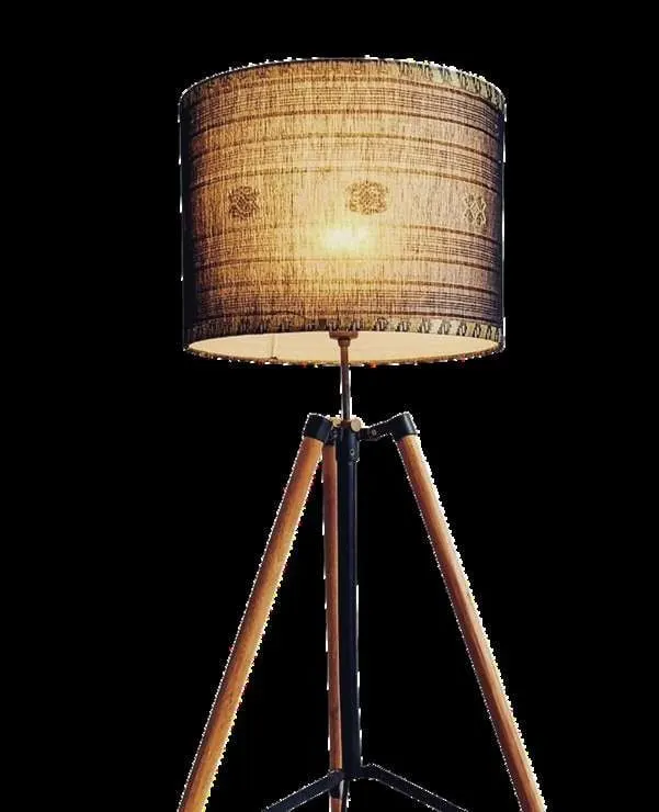 Lampu berdiri berkaki tripod kayu dengan kap lampu dari kain tenun cokelat yang menyala