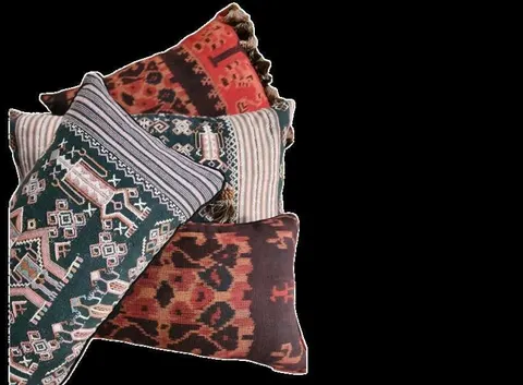 Tumpukan sarung bantal dari kain tenun motif merah, hijau tua dan garis abu-abu di latar hitam
