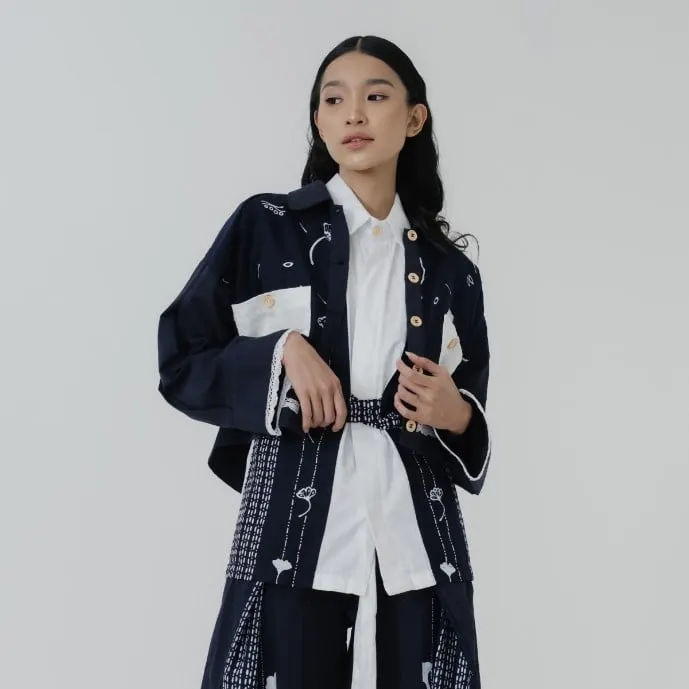 Model memakai outer biru tua bermotif batik putih di atas kemeja putih dengan obi kain