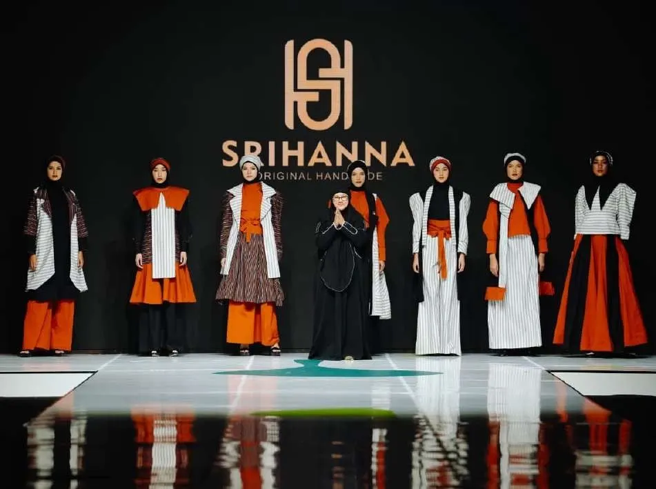 Deretan model di panggung peragaan busana memakai busana muslim lurik putih, oranye dan hitam di depan logo Srihanna
