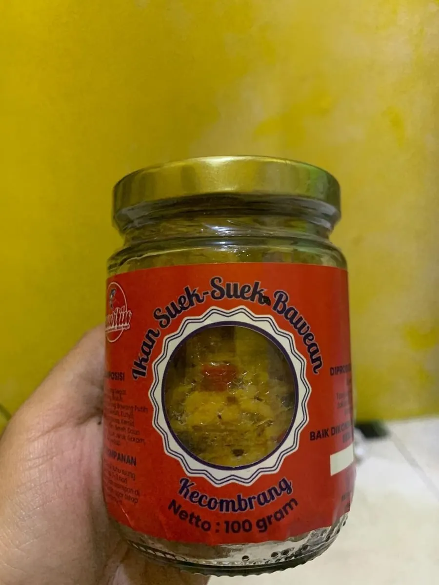 Tangan memegang toples Ikan Suek-Suek Bawean varian Kecombrang berlabel oranye di depan dinding kuning