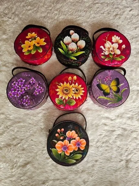 Tujuh tas bulat berwarna merah, ungu dan hitam dengan lukisan bunga dan kupu-kupu di atas karpet bulu putih