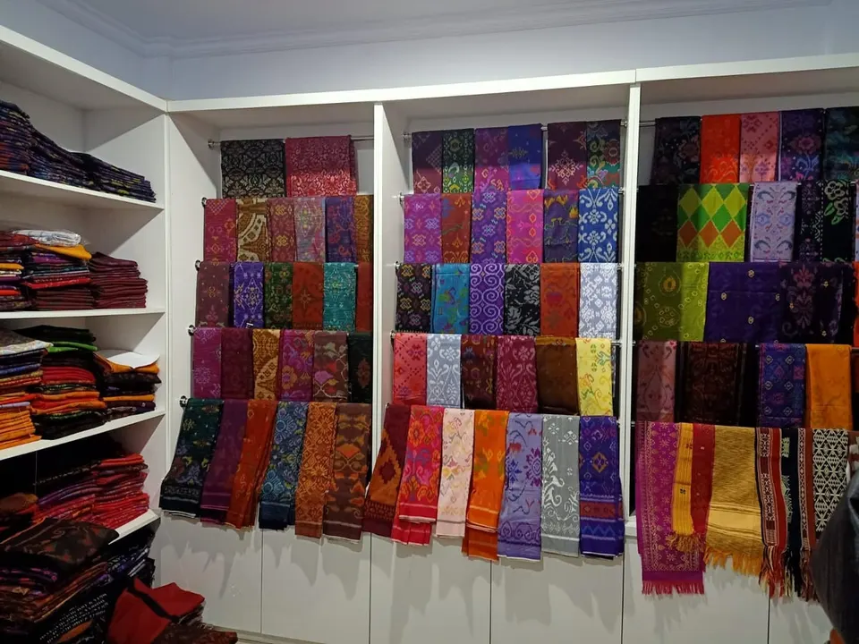 Rak toko berisi deretan kain tenun dan selendang warna-warni yang dilipat dan digantung