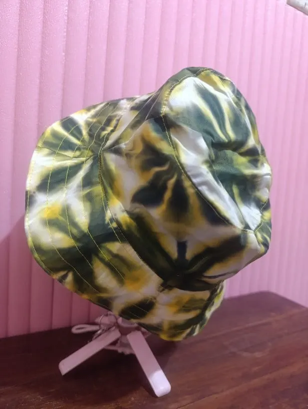 Topi bucket bermotif shibori hijau tua, kuning dan putih pada dudukan topi