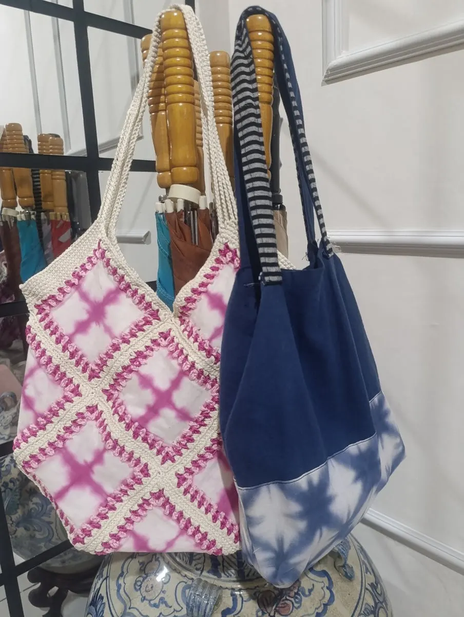 Tas bahu shibori merah muda berbingkai rajutan dan tas kain biru tua bermotif shibori biru putih tergantung