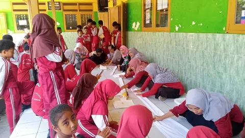 Siswa berseragam merah dan pendamping melipat kain putih di lantai teras sekolah saat workshop