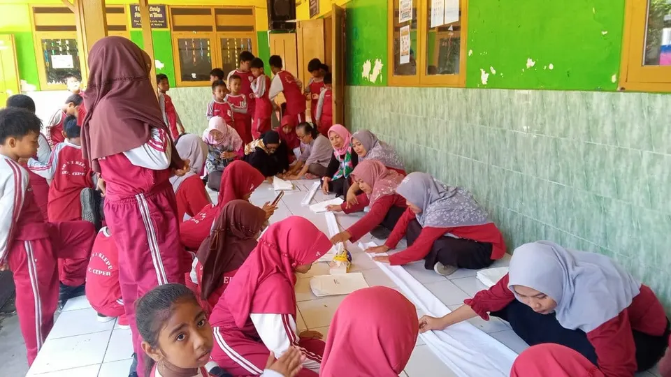 Siswa berseragam merah dan pendamping melipat kain putih di lantai teras sekolah saat workshop