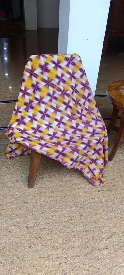 Kain bermotif shibori ungu dan kuning tersampir di sandaran kursi kayu