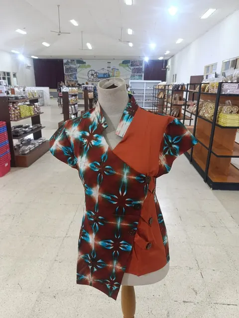 Atasan shibori cokelat kemerahan bermotif biru dan putih dengan panel jingga pada manekin di dalam toko