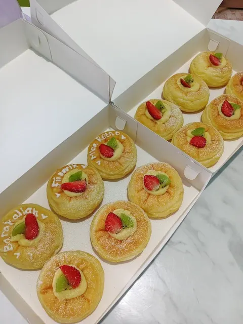 Dua kotak putih berisi donat krim vla dengan potongan stroberi dan kiwi, beberapa bertuliskan ucapan dari krim