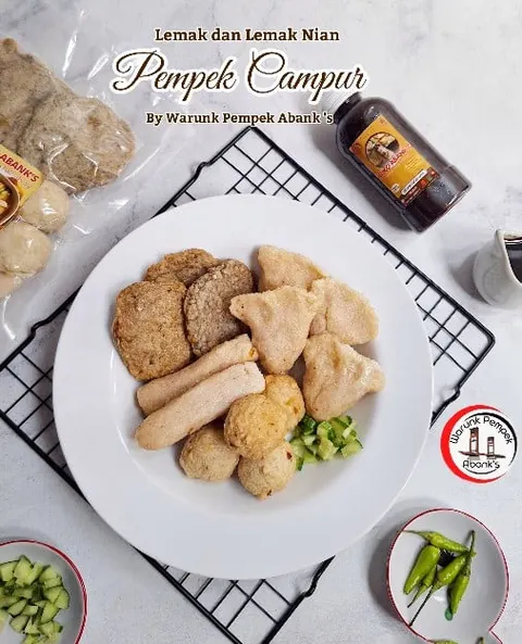 Piring putih berisi pempek campur dan potongan mentimun dengan botol cuko, bertulisan Pempek Campur