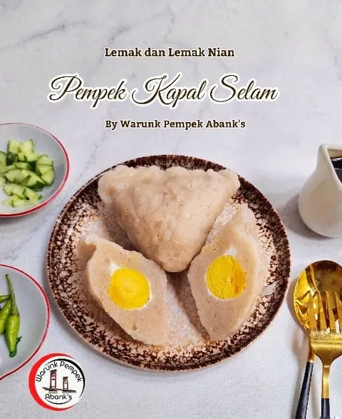 Pempek kapal selam dibelah dua memperlihatkan kuning telur di atas piring, bertulisan Pempek Kapal Selam