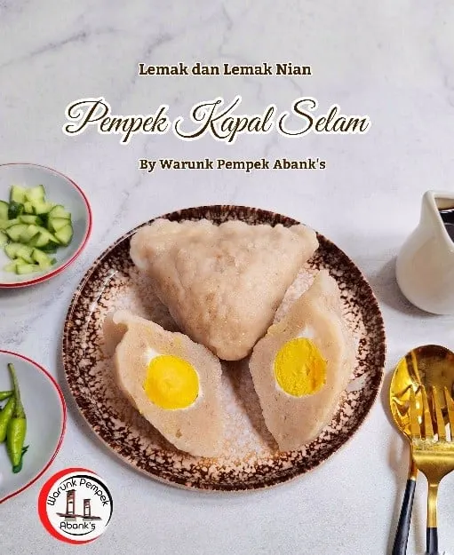 Pempek kapal selam dibelah dua memperlihatkan kuning telur di atas piring, bertulisan Pempek Kapal Selam