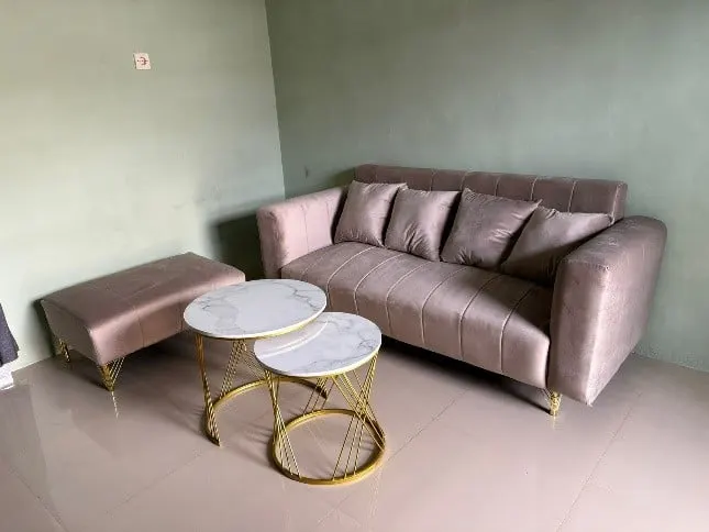 Sofa tiga dudukan merah muda dengan bantal, puf dan dua meja bundar marmer di ruangan hijau muda
