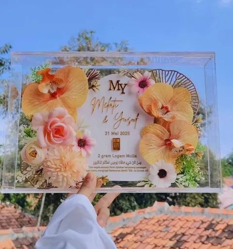 Bingkai akrilik bening berisi bunga hias oranye dan merah muda, nama pengantin dan logam mulia 2 gram