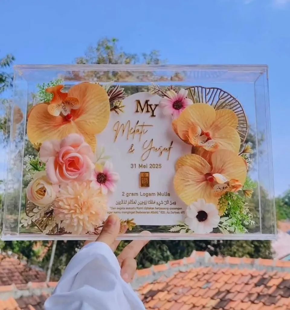 Bingkai akrilik bening berisi bunga hias oranye dan merah muda, nama pengantin dan logam mulia 2 gram
