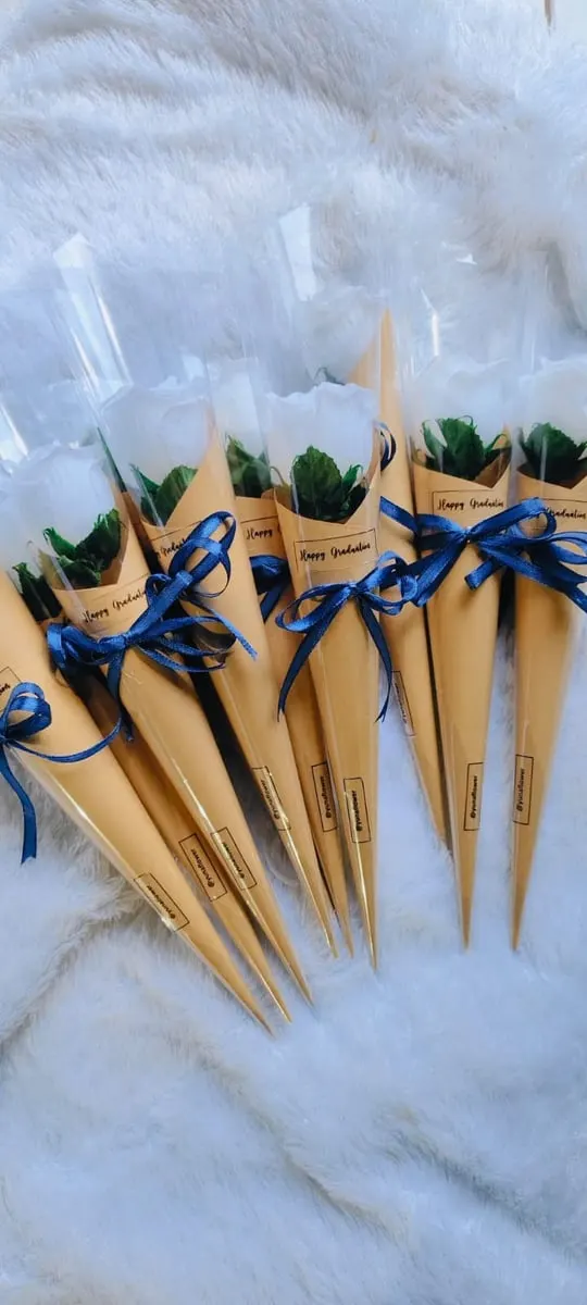 Deretan buket bunga putih satuan dalam kerucut kertas kraft berpita biru bertulisan Happy Graduation