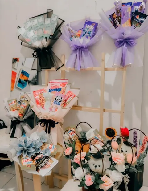 Rak kayu dengan buket uang, buket snack berbungkus ungu dan putih, serta buket boneka dan bunga rajut